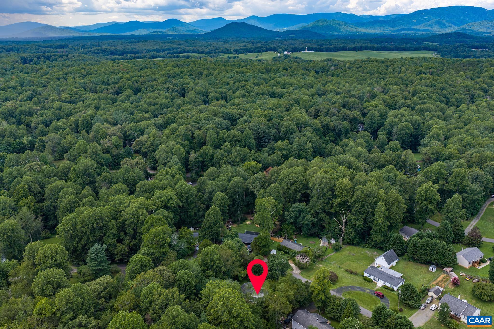 Spectacular aerial view capturing the home's prime location surrounded by dense forest canopy and distant mountain ridge views! A perfect blend of secluded country privacy, natural beauty, and scenic mountain views right from home.