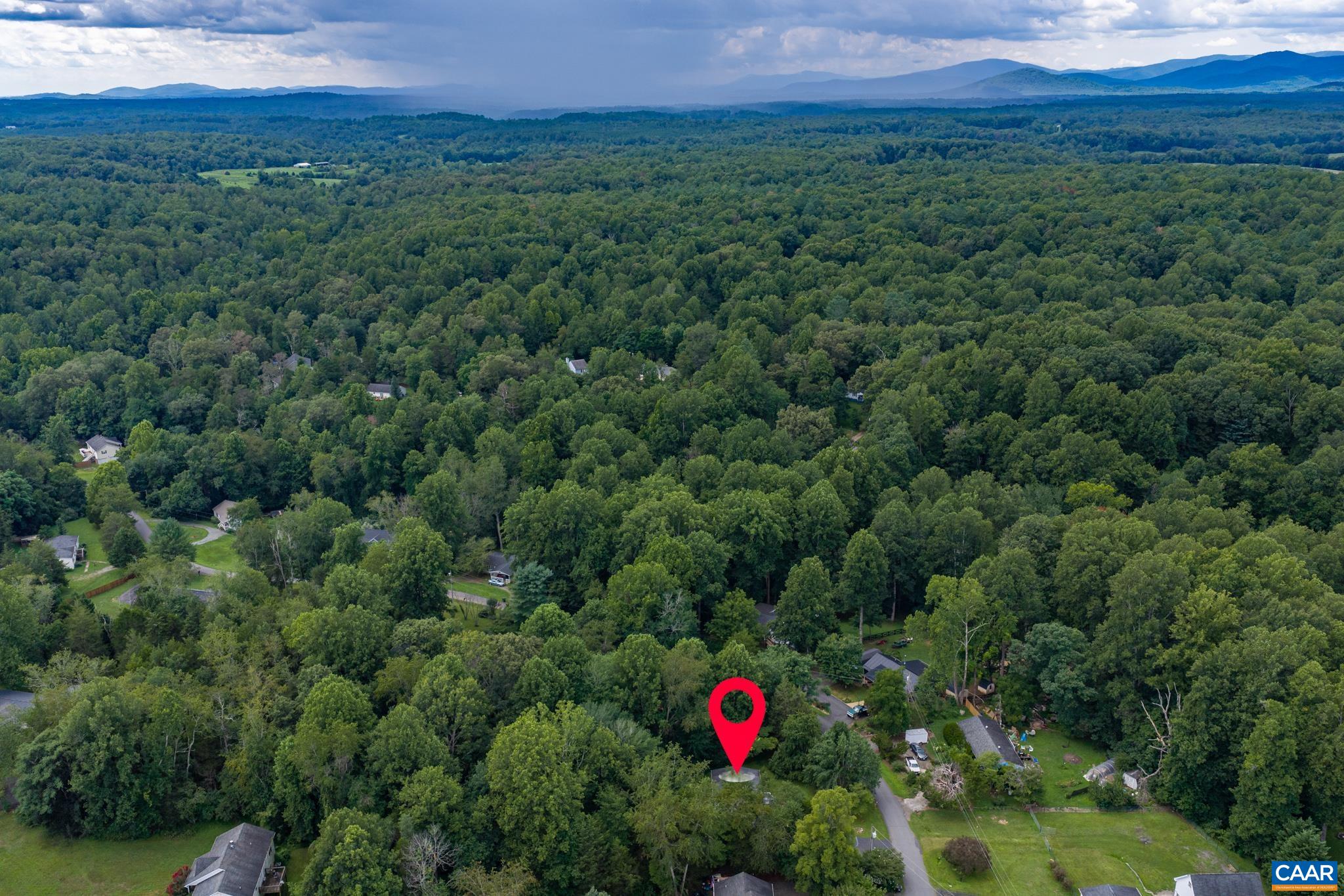 Expansive aerial shot highlighting the home's exact pin-pointed location nestled among lush, dense treetops! Sweeping mountain vistas and rolling green hills create a private, tranquil sanctuary with unbeatable natural scenery.