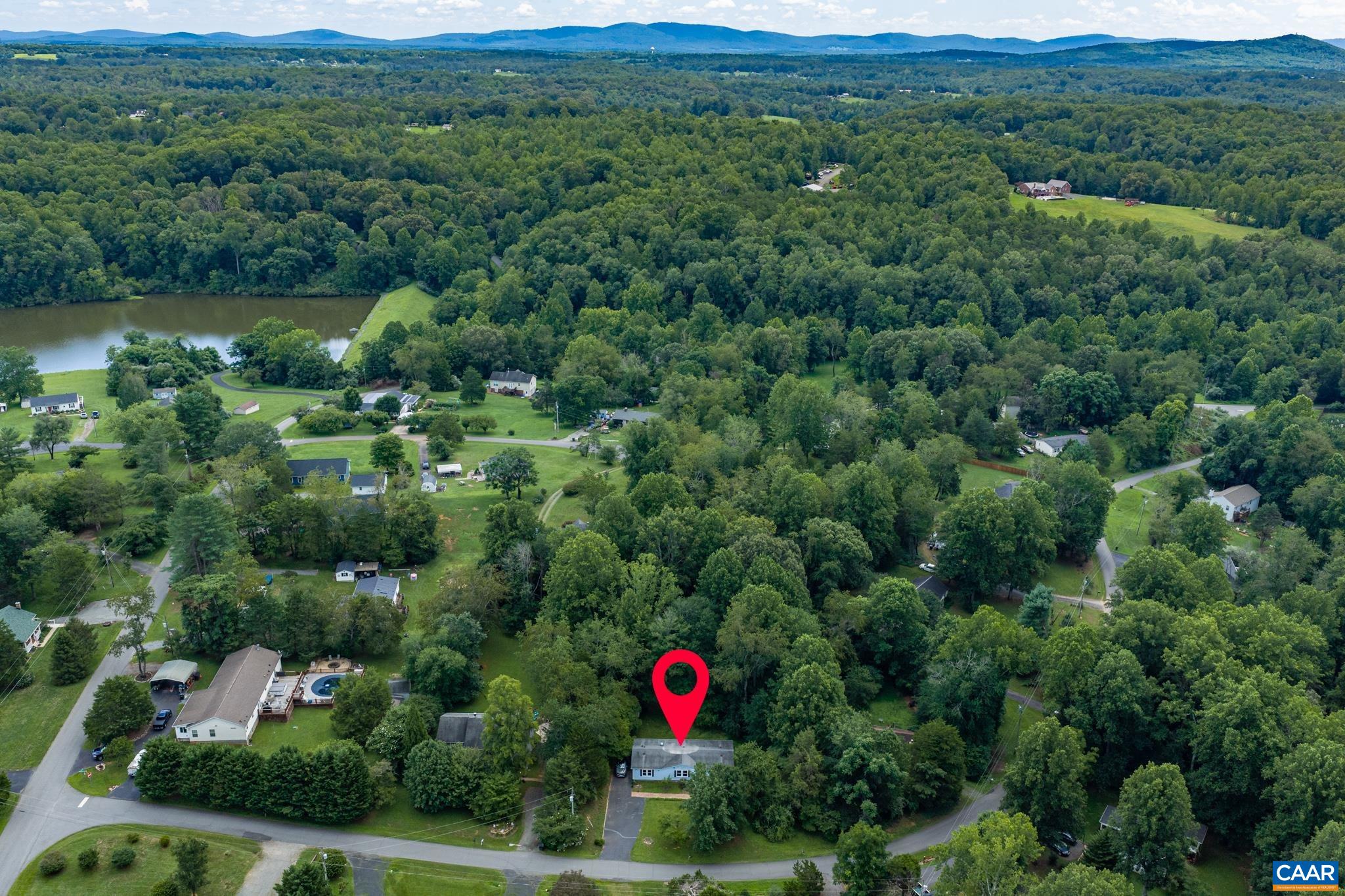 Pinpointed in a peaceful neighborhood setting! This aerial view showcases the home's lush, tree-lined lot, nearby water features, and scenic distant hills. Enjoy a tranquil community lifestyle surrounded by nature's beauty!