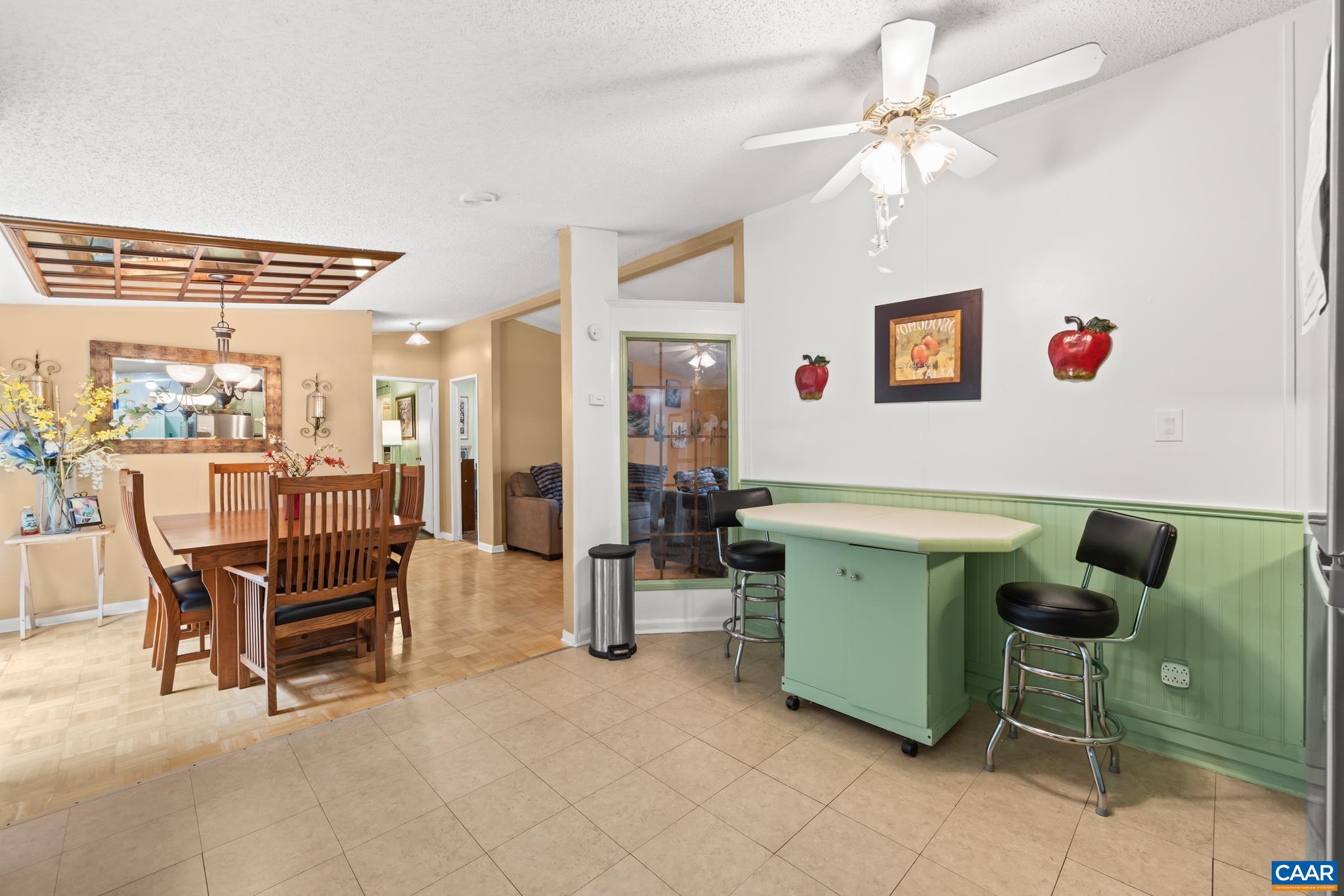 Versatile eat-in kitchen and breakfast nook space! Features a convenient island/bar with seating, charming sage green wainscoting, and a ceiling fan, opening effortlessly into the dining area. Perfect for quick meals or informal gathering!