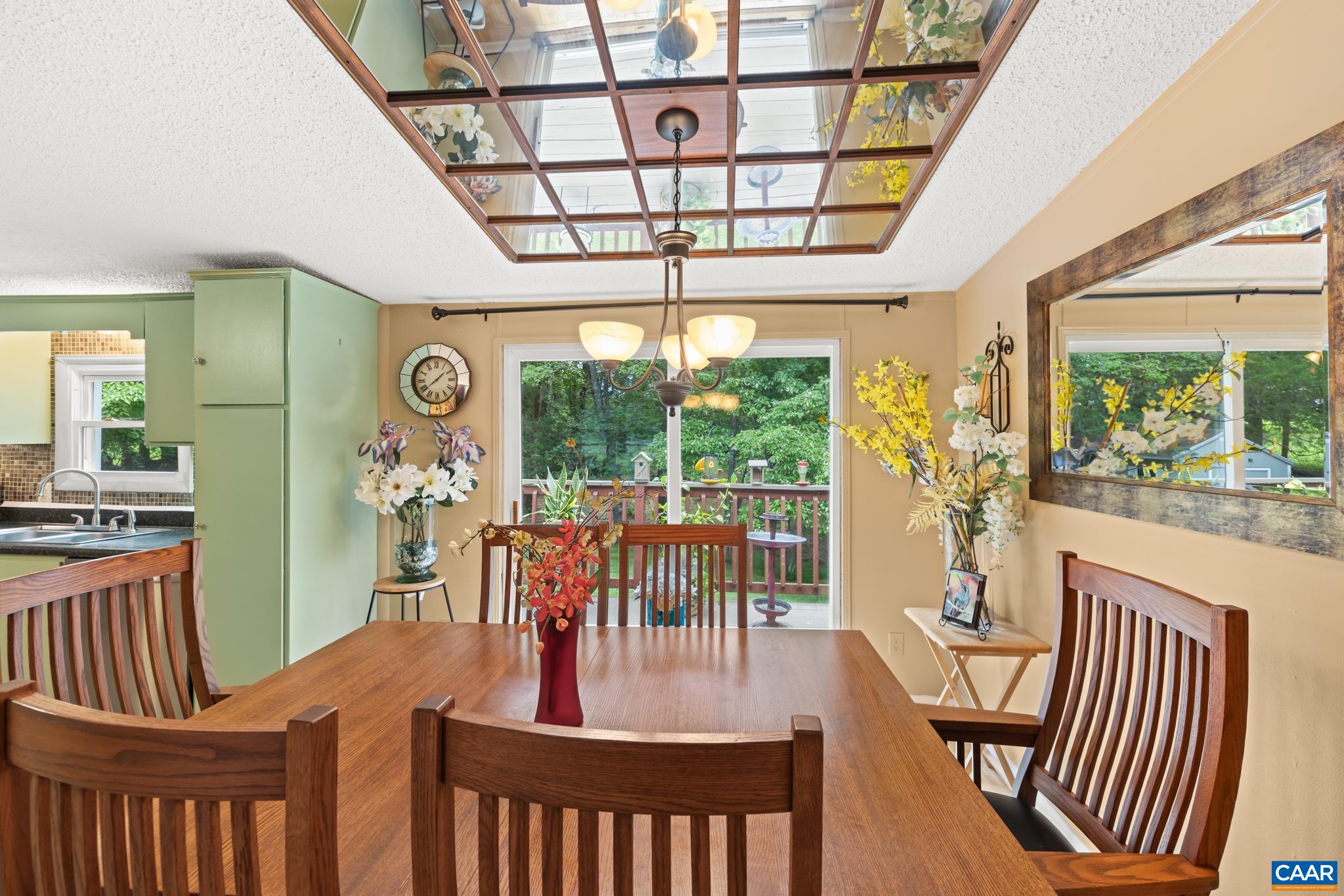 Dine with a view! This inviting dining room features warm wood accents, unique ceiling detailing, and sliding glass doors opening directly onto a deck surrounded by greenery. Enjoy seamless indoor-outdoor living and effortless entertaining!