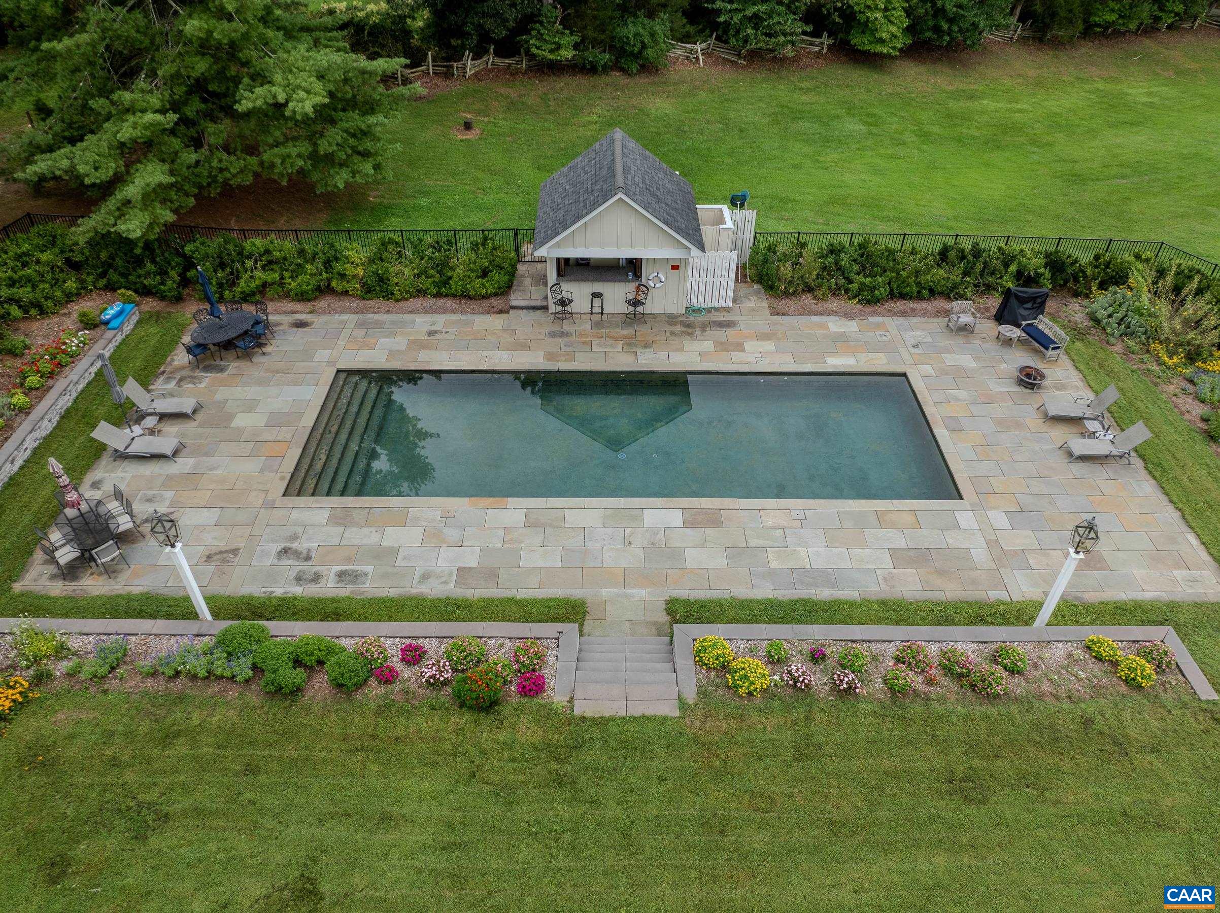 Heated in-ground pool with pool house is surrounded by slate pool deck.