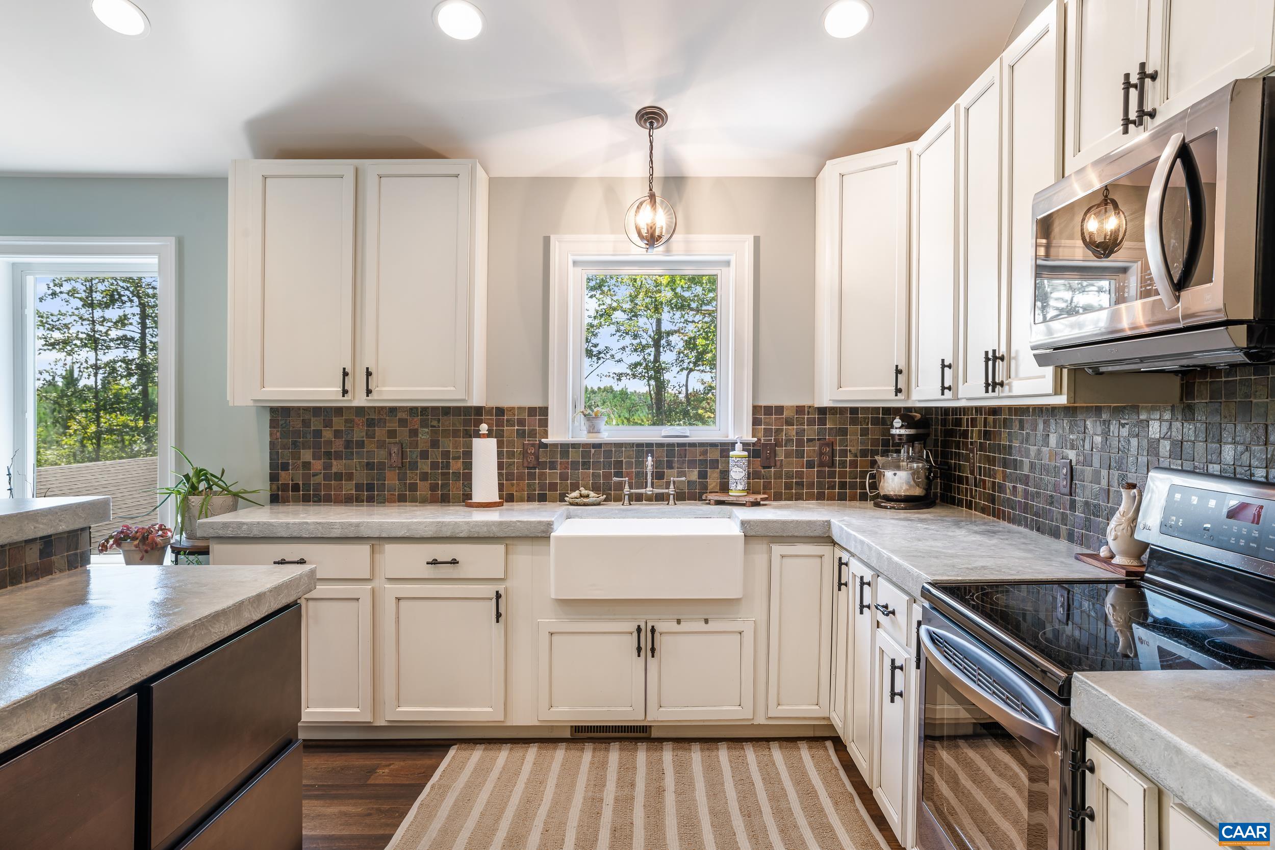 Apron-Front porcelain sink beneath the window, surrounded by concrete countertops, white cabinetry and backsplash Apron-Front porcelain sink beneath the window, surrounded by concrete countertops, white cabinetry and backsplash