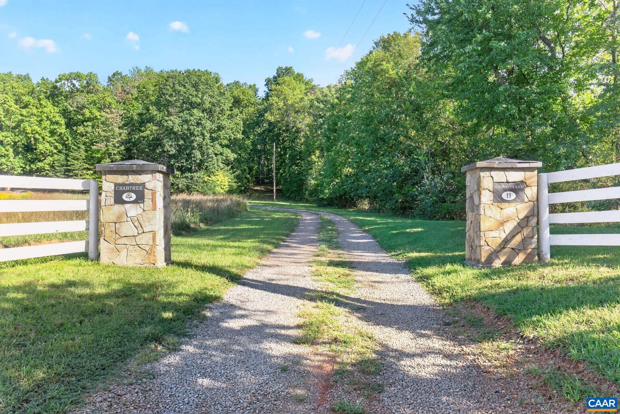 The entrance, off of a Scenic Byway, has four board white fencing across the front and stone pillars.