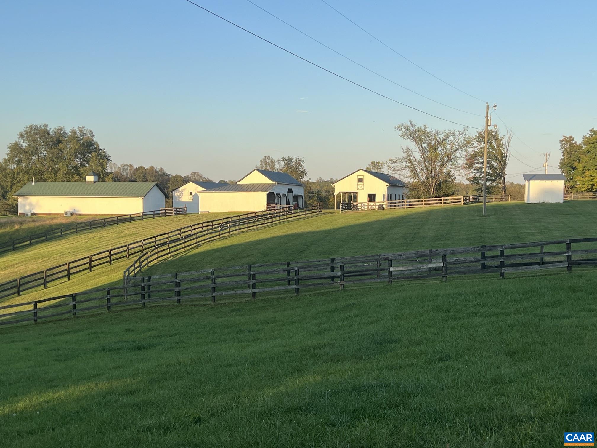 View of the barn complex among the paddocks: the original six-stall barn with office and tack room, the four-bay barn built in 2013, and the equipment barn. View of the barn complex among the paddocks: the original six-stall barn with office and tack room, the four-bay barn built in 2013, and the equipment barn.