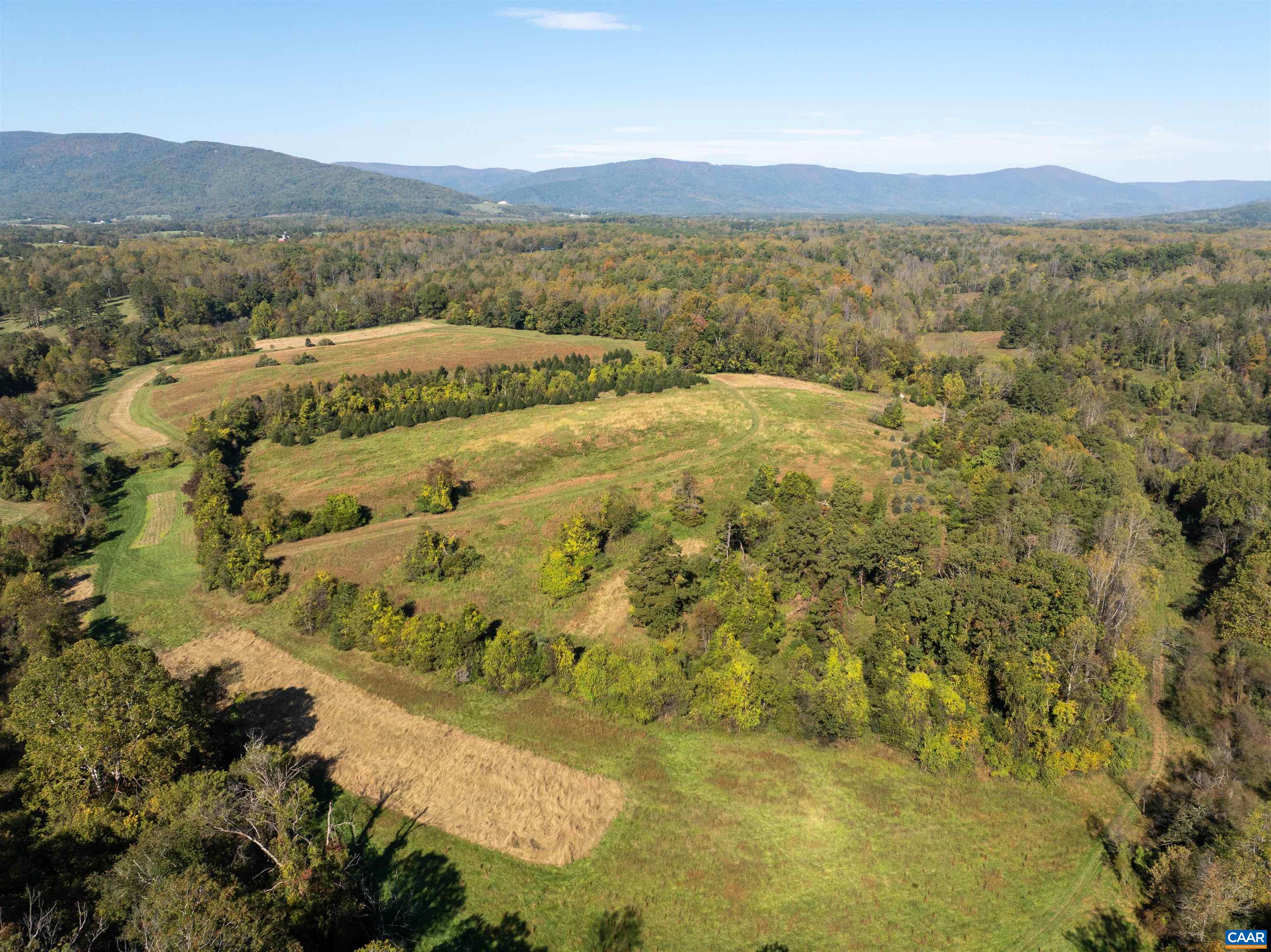 The upper fields from above: open meadow framed by hardwoods, with a mown trail loop around the perimeter and the mountains beyond. The upper fields from above: open meadow framed by hardwoods, with a mown trail loop around the perimeter and the mountains beyond.
