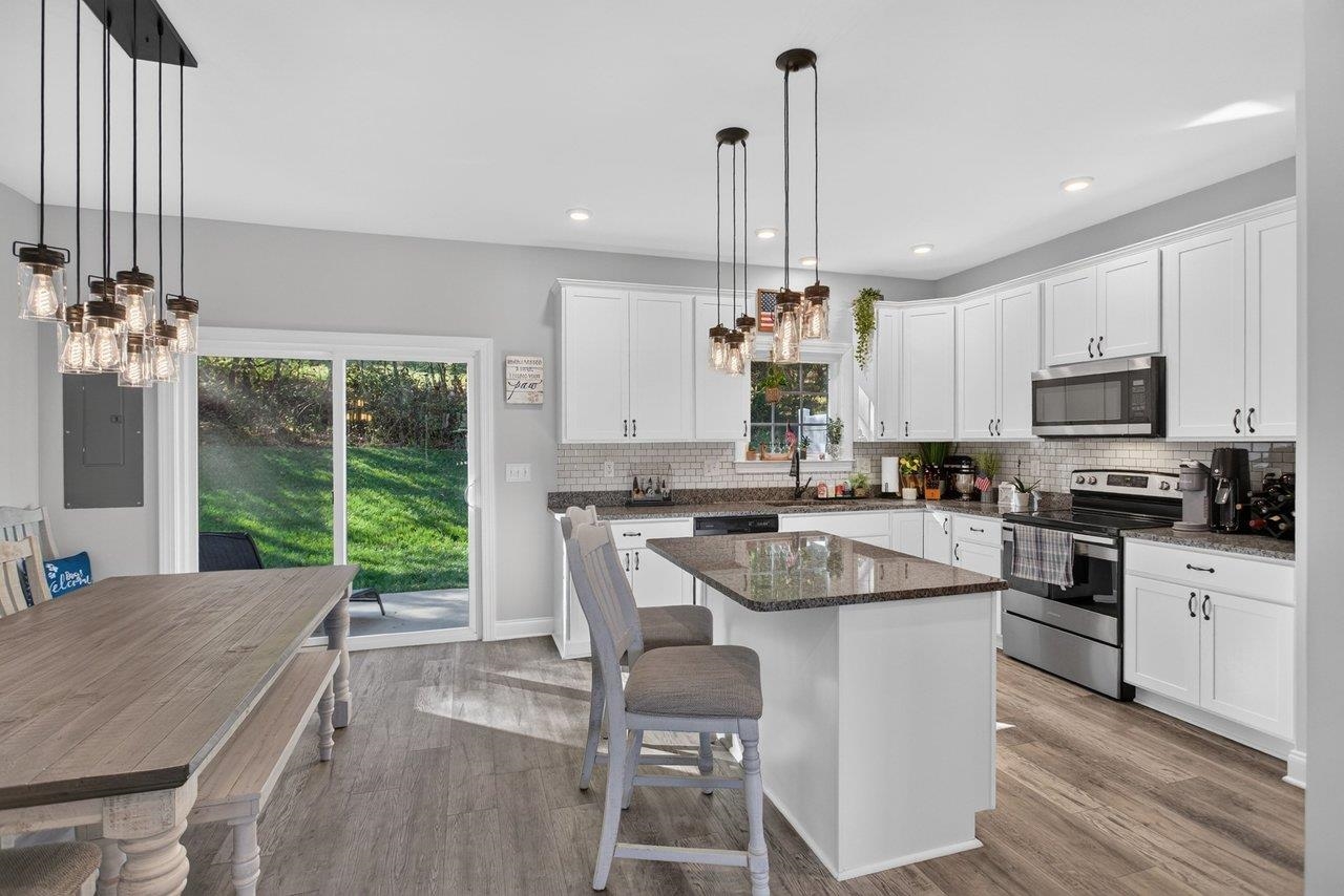 The bright kitchen features white cabinetry, granite countertops, an island with additional seating, stainless steel appliances, a pantry, LVP floors, and plenty of natural light.