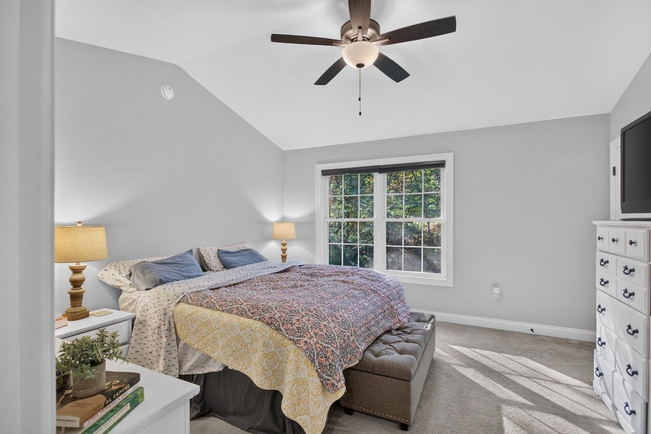 The spacious primary bedroom features a cathedral  ceiling, warm carpeting, a walk-in closet, ceiling fan, and a private bath.