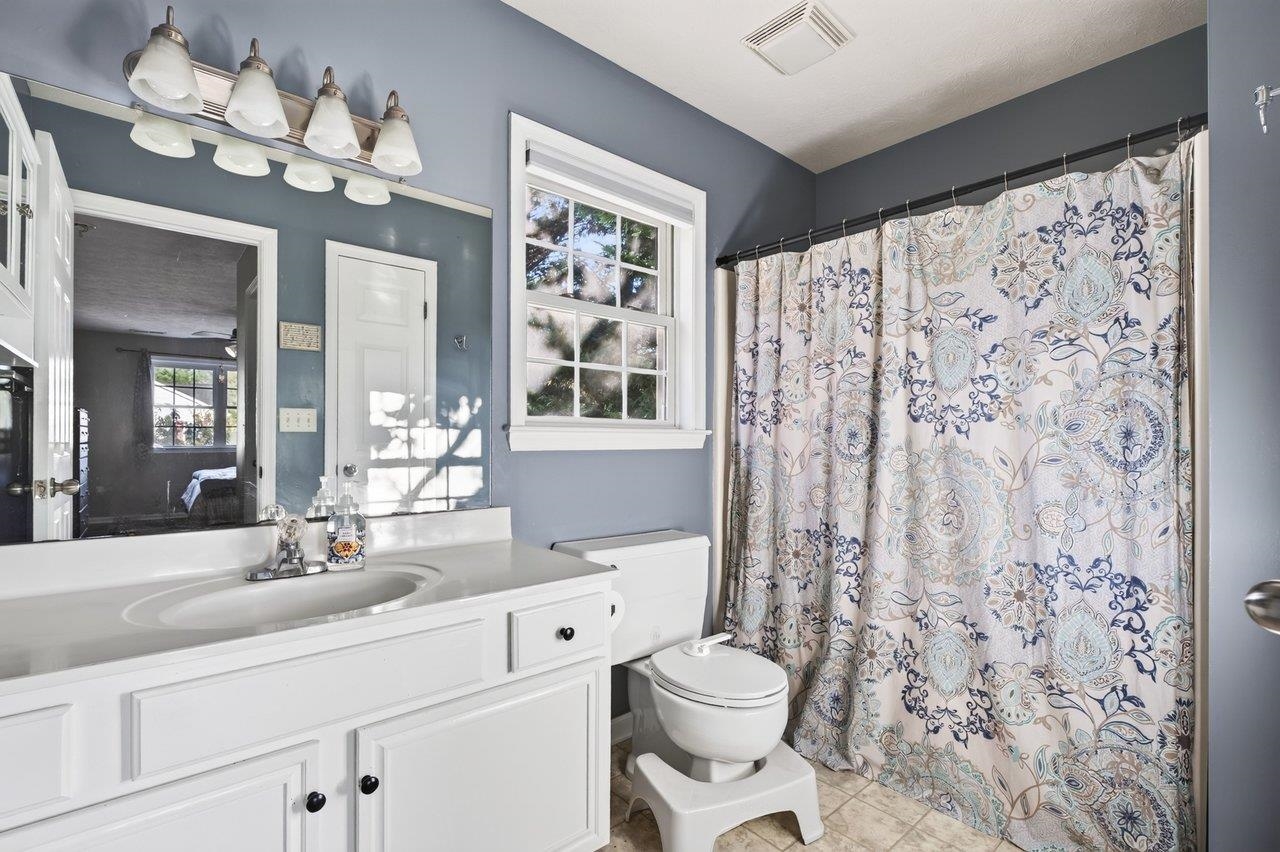 The primary bath features vinyl flooring, a white vanity, a tub/shower combination, and a window that provides natural light.